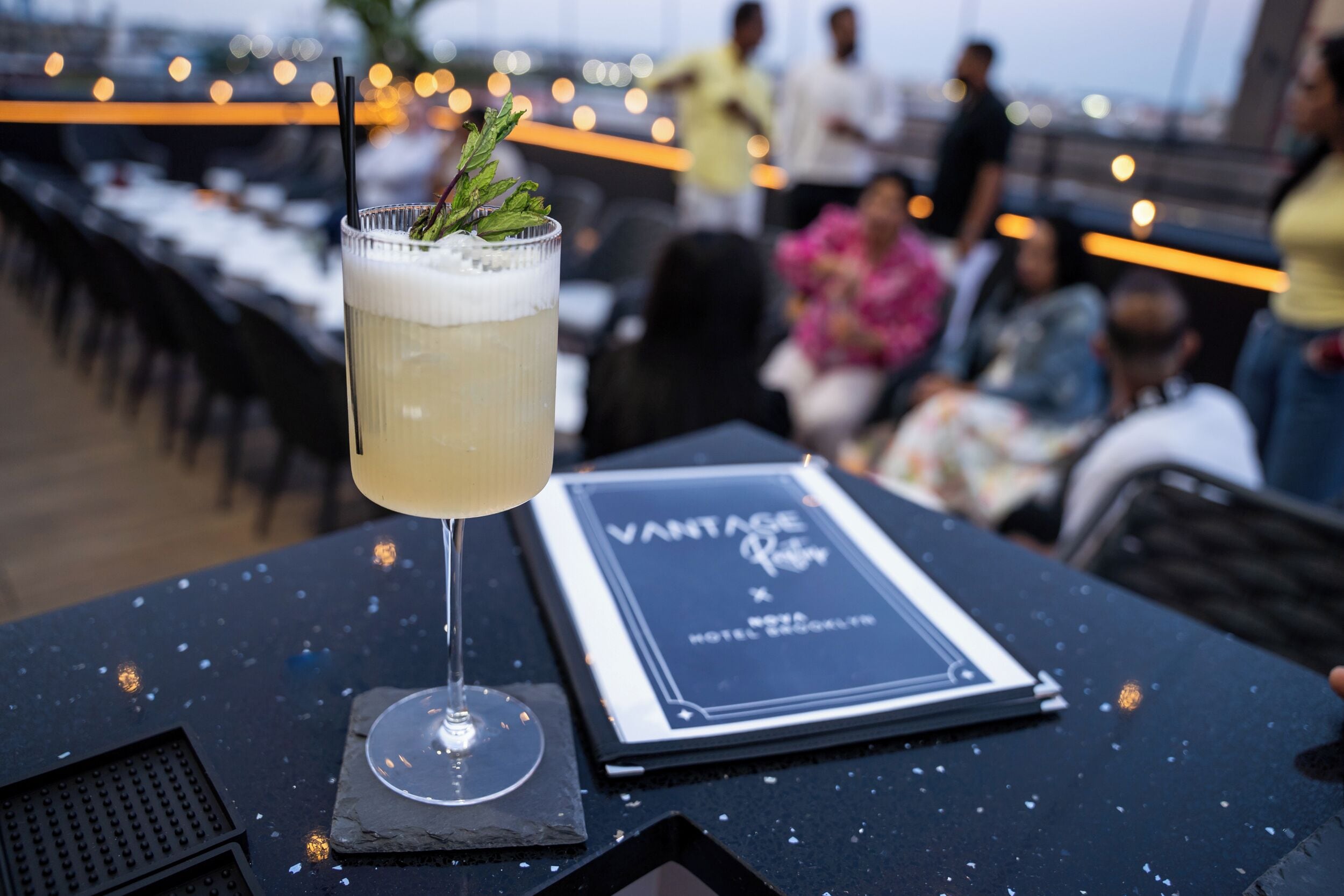 A cocktail glass with a mint garnish on a table with a menu titled "VANTAGE".