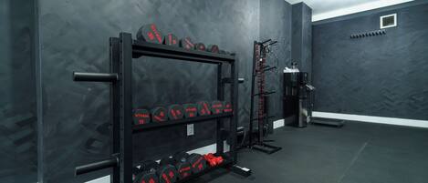 A gym with a weight rack, dumbbells, and a squat rack.