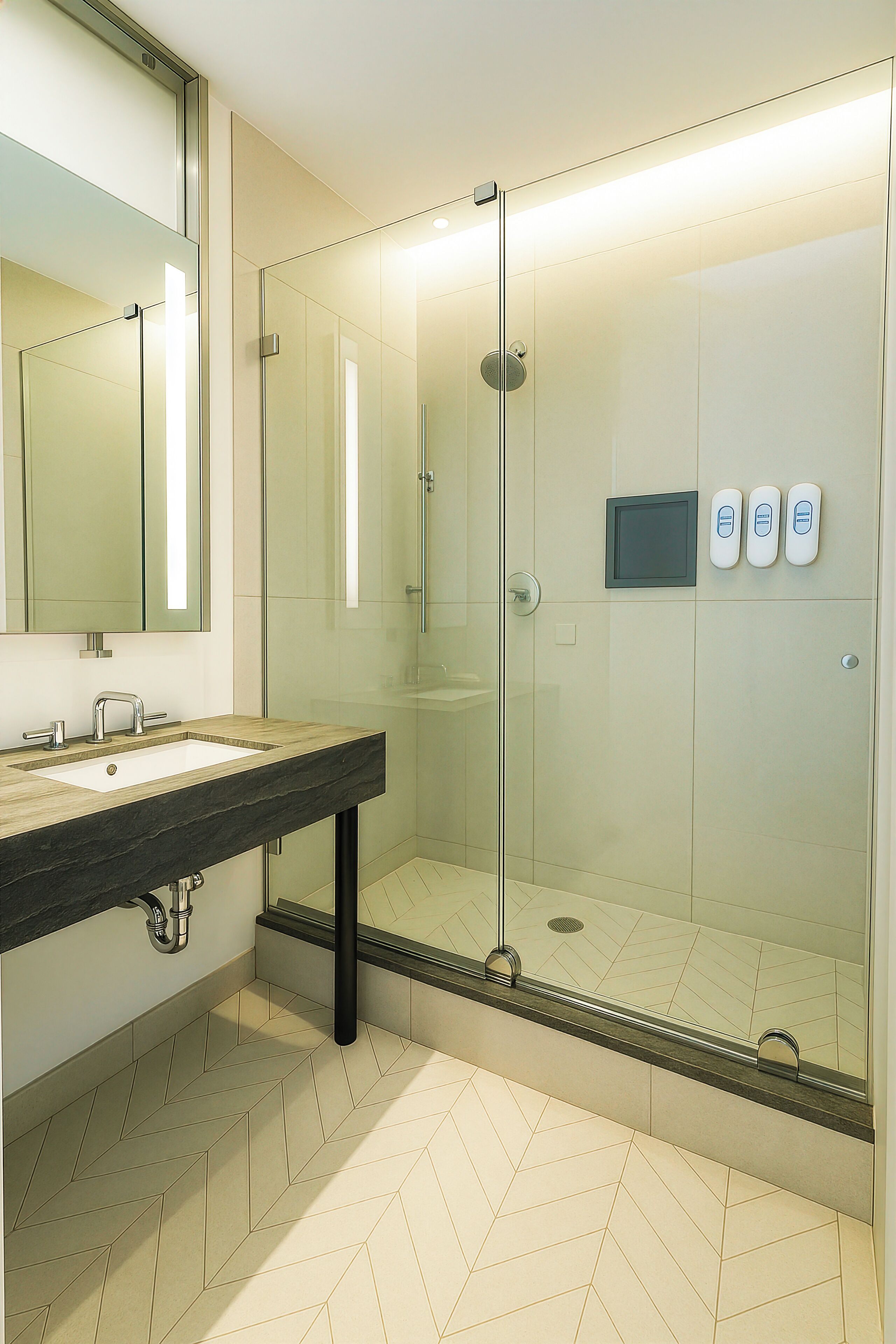 A modern bathroom with a glass-enclosed shower, a sink with a marble countertop, and a large mirror.
