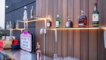 Un espace bar avec différentes bouteilles d’alcool et des verres, une enseigne indiquant « BIENVENUE AU VANTAGE ROOFTOP », et un mur en bois en arrière-plan.