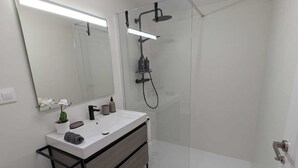 A modern bathroom with a glass-enclosed shower, a white sink with a black faucet, and a large mirror. - Casa Fita Santillana del Mar  (Santillana del Mar)