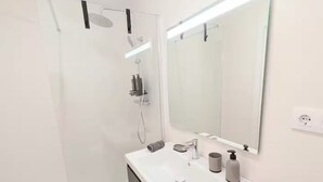Casa de banho moderna com lavatório branco, móvel escuro e um espelho grande.