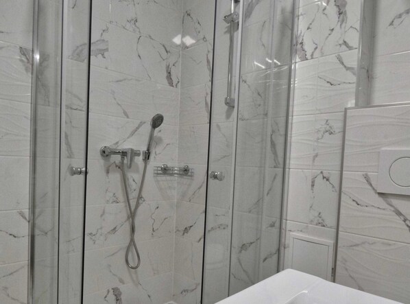 A bathroom with a glass-enclosed shower, marble tiles, and a white sink.