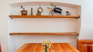 Une table à manger en bois, ornée d’un vase de fleurs au centre. Au-dessus de la table, on trouve deux étagères en bois sur lesquelles sont disposés divers objets, notamment une bouteille de vin et un objet décoratif.