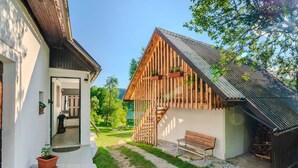 Une maison moderne avec une façade en bois, un petit porche et un jardin agrémenté d’un banc et de plantes en pot.