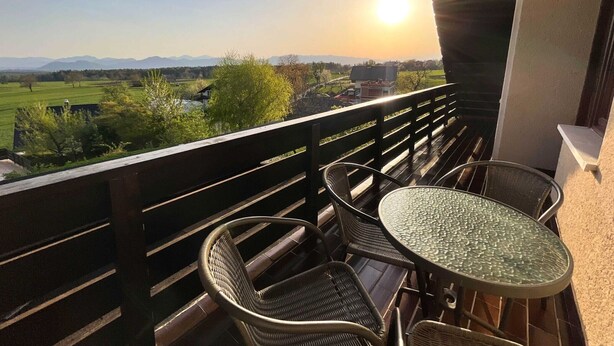 Un balcon agrémenté de fauteuils en osier et d’une table en verre, offrant une vue sur un paysage verdoyant et des montagnes.