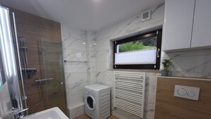 A modern bathroom with a glass shower enclosure, a built-in washing machine, a radiator, and a television mounted above the radiator.