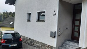 A building with a stone facade, a black car parked in front, and a wooden door with a metal handle.