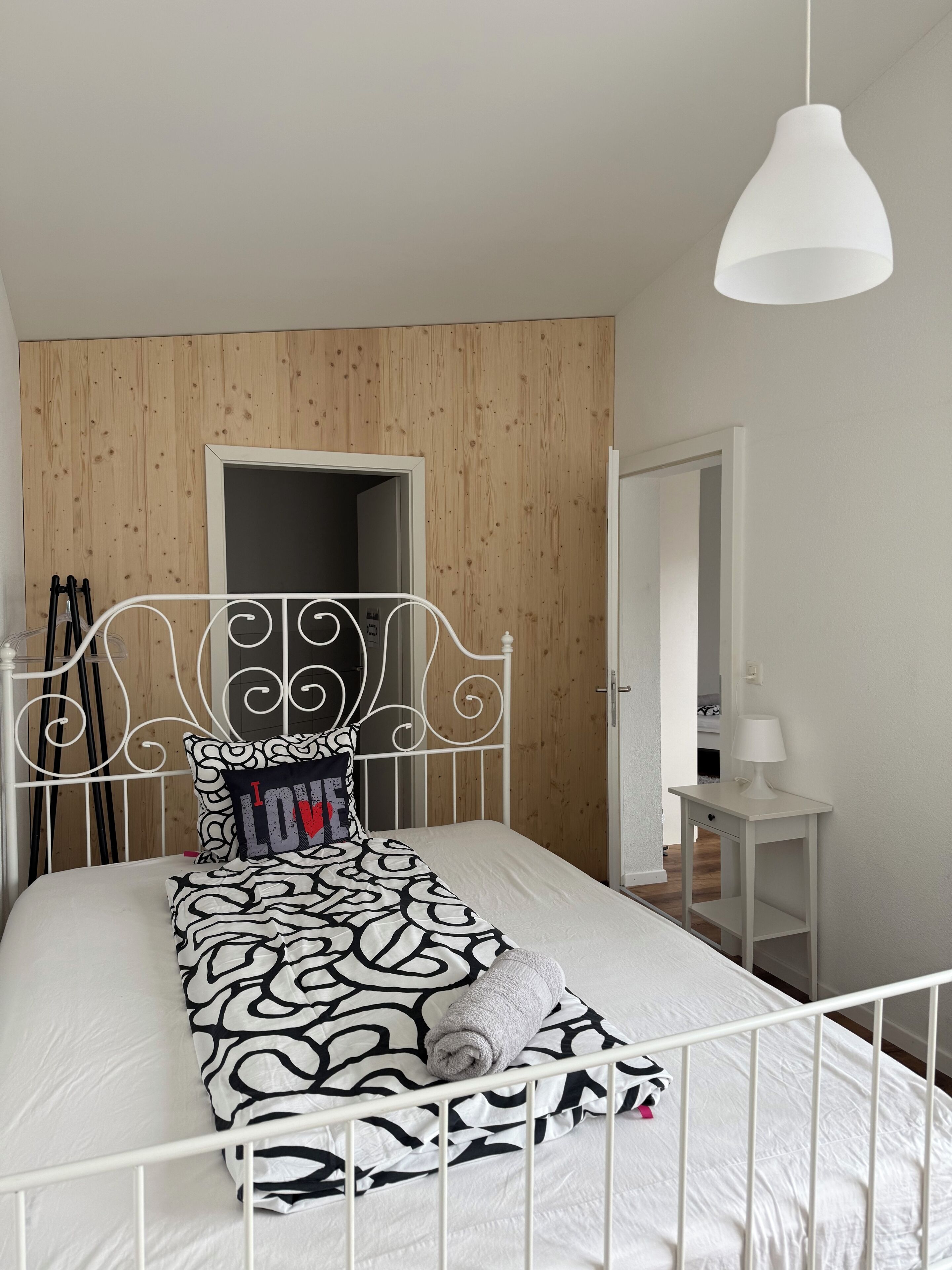 A neatly made bed with a patterned bedspread, a decorative headboard, and a hanging pendant light.