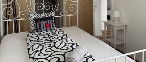 A neatly made bed with a patterned bedspread, a decorative headboard, and a hanging pendant light.