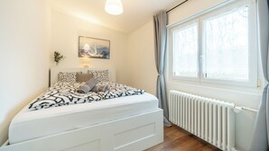 A bedroom with a bed, a radiator, a window with curtains, and a hanging light fixture.