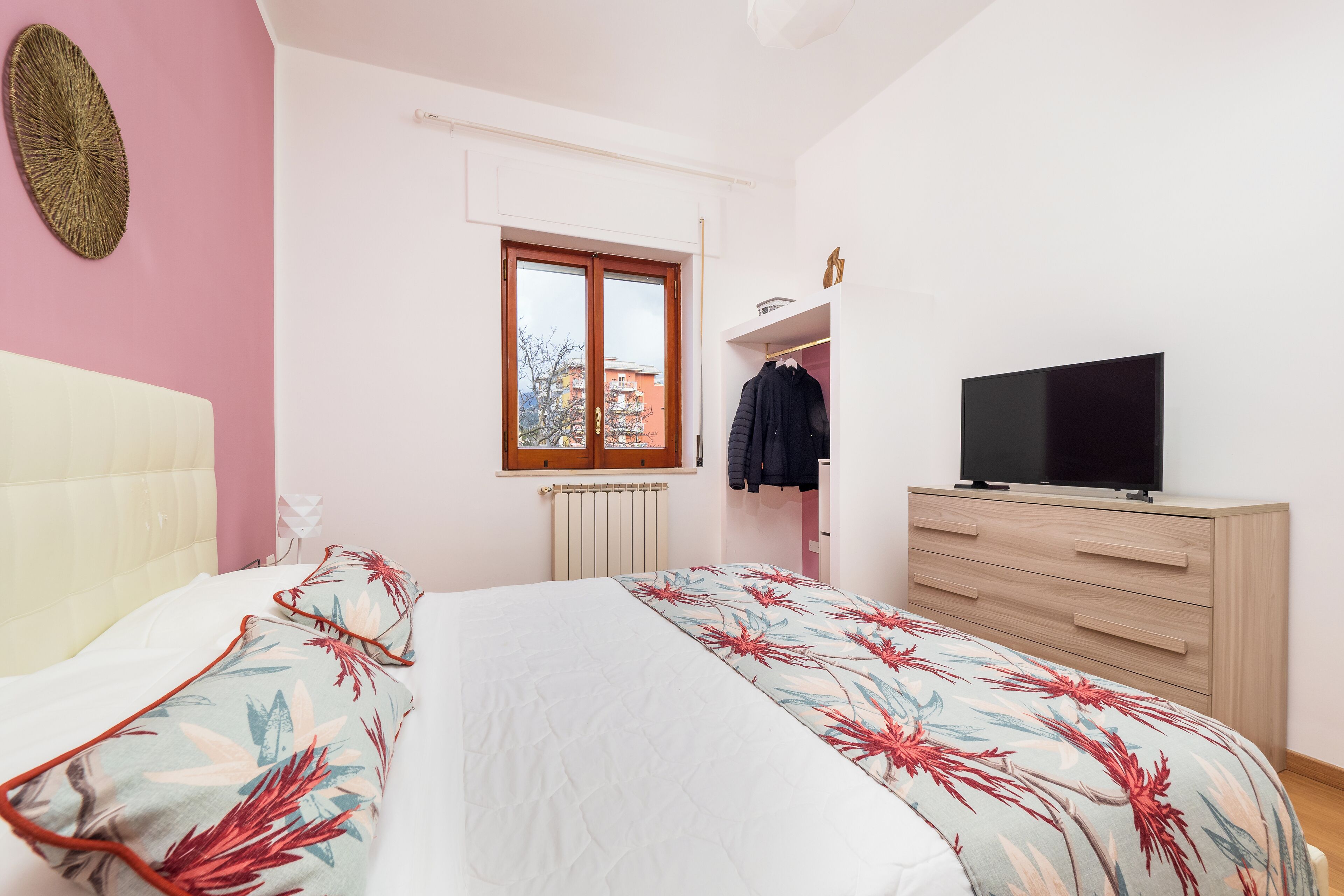 Een slaapkamer met een bed, een televisie op een dressoir, een raam en een radiator.
