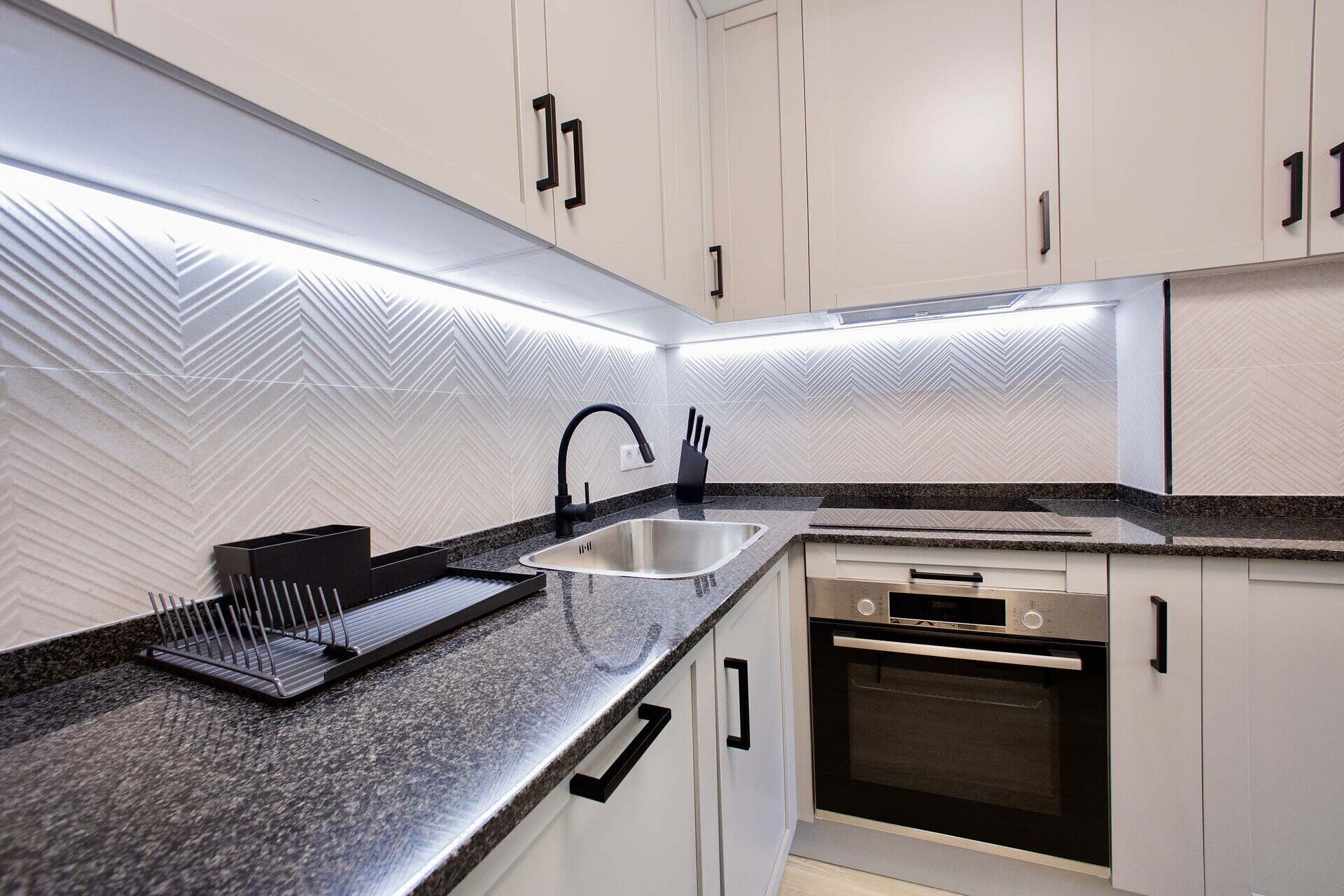 Una cocina moderna con encimera de granito, pileta de acero inoxidable y horno integrado.