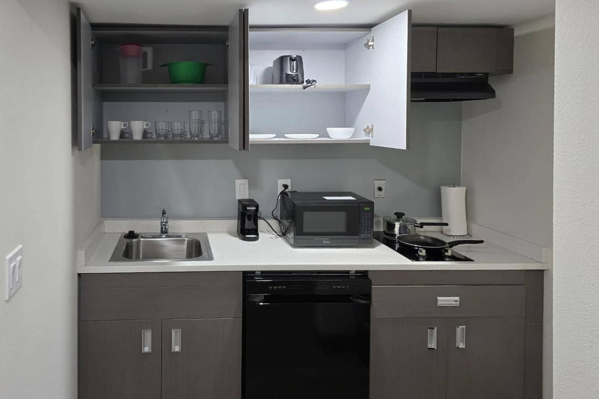 A compact kitchen with a built-in dishwasher, a microwave, a coffee maker, and a stovetop.