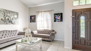 Ein Wohnzimmer mit einem gesteppten Sofa, einem Glastisch und einem gemusterten Teppich.