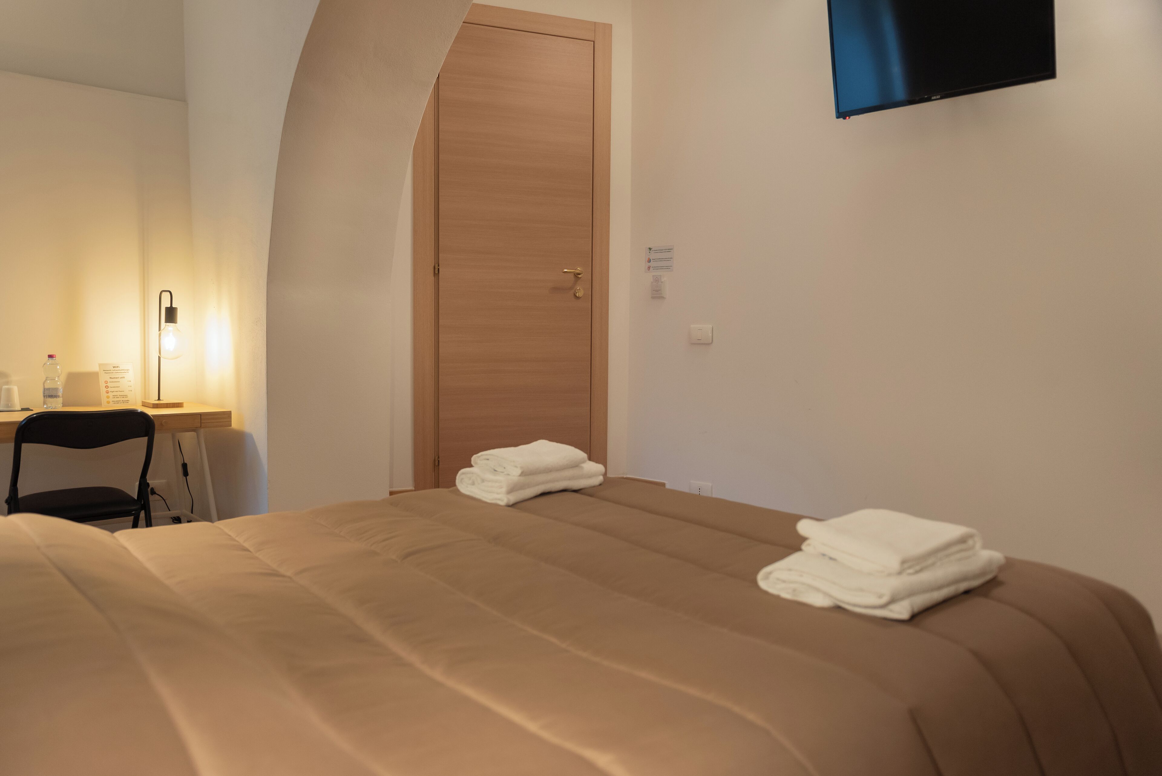A hotel room with a bed, a desk, a chair, a TV, and a door.