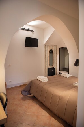 Quarto com cama, televisão na parede, espelho e guarda-roupa.