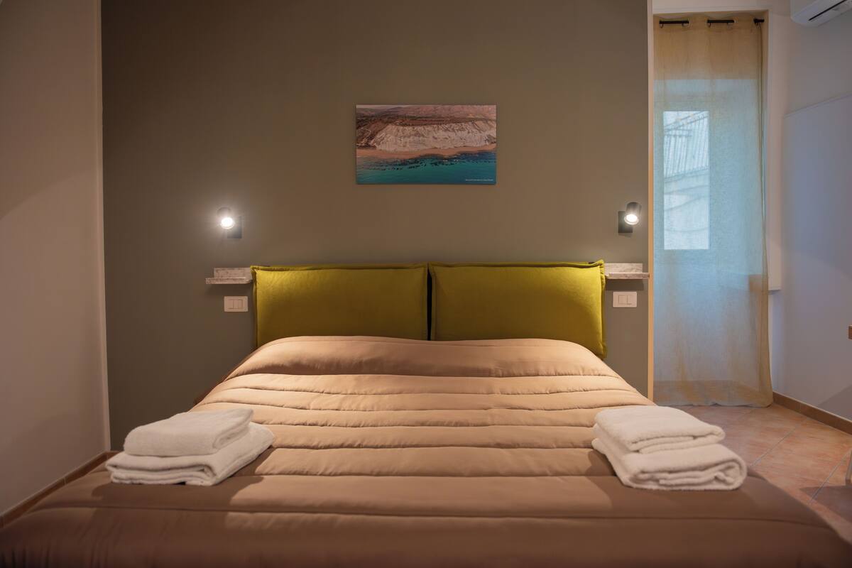 A neatly made bed with two pillows, a wall-mounted painting, and two bedside lamps.