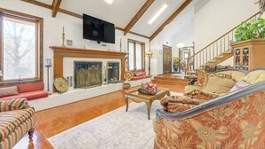 Ein geräumiges Wohnzimmer mit Kamin, einem an der Wand montierten Fernseher und einer Treppe, die in einen oberen Stock führt.