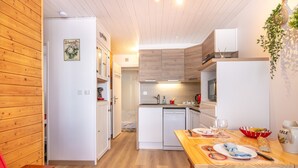 A compact kitchen with wooden cabinets, a dishwasher, and a dining area with a table set for two. - Le Bleuet - Vue montagne, pistes accessibles à pied (Chamrousse)