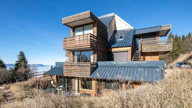A modern multi-level house with wooden exterior and large windows, situated on a grassy hill with a view of the ocean. - Le Bleuet - Vue montagne, pistes accessibles à pied (Chamrousse)