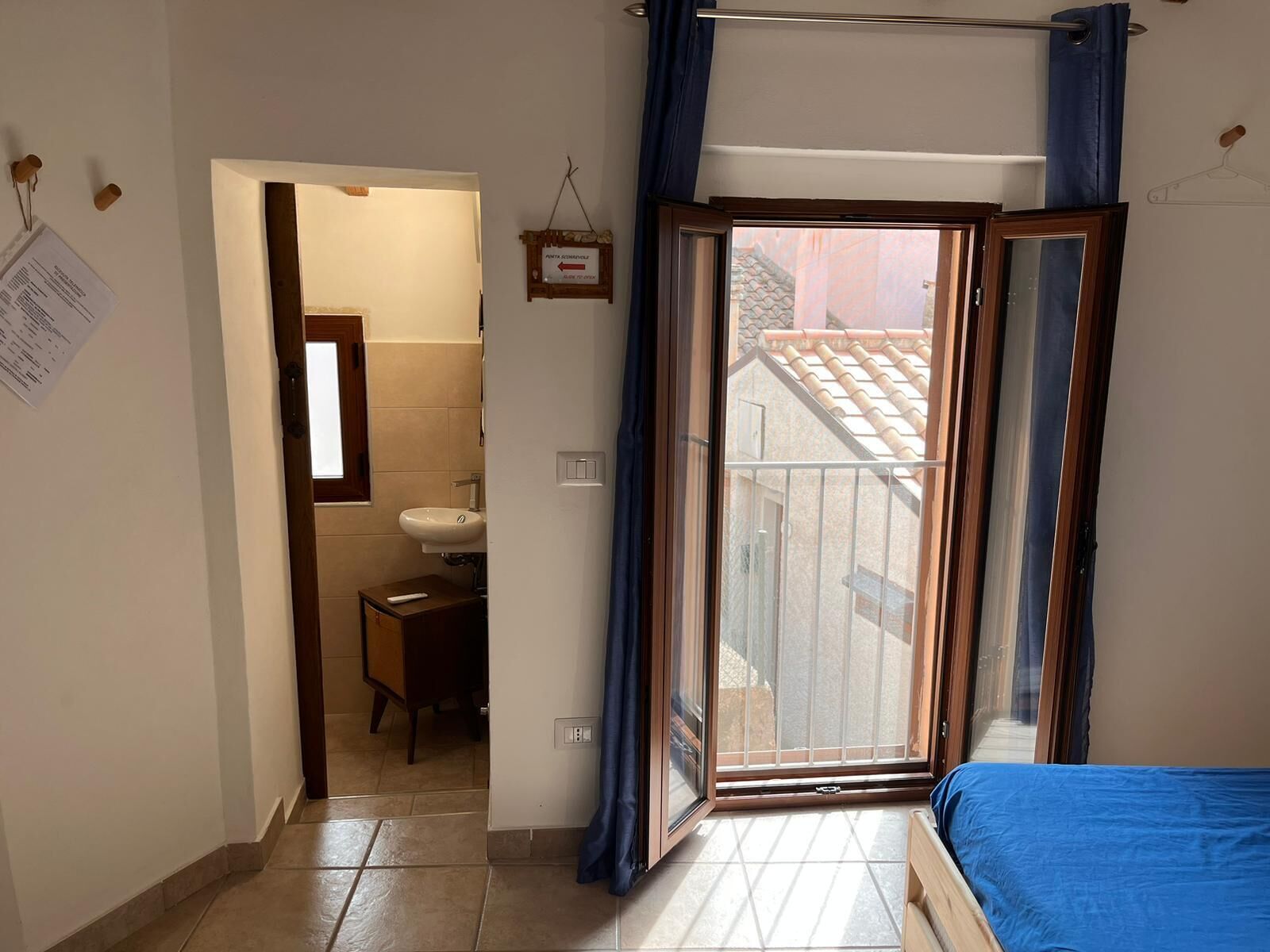 Ein Schlafzimmer mit Bett, ein Badezimmer mit Waschbecken und Blick ins Freie durch eine Schiebetür.