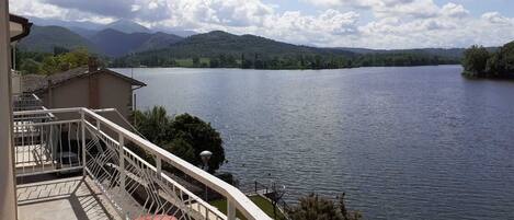 A balcony with a view of a lake, mountains in the background, and a red car parked nearby.
