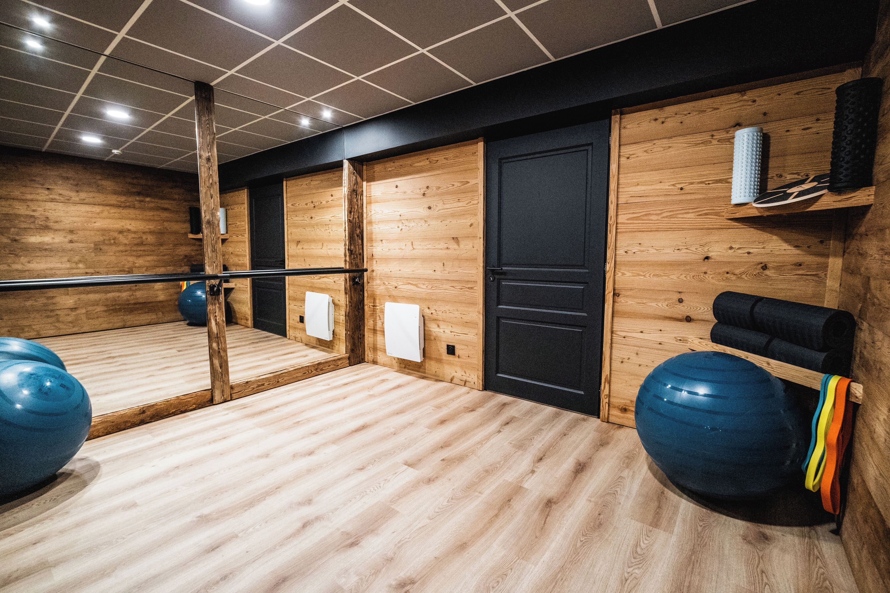Un gimnasio con paredes de madera, un espejo grande, pelotas de ejercicio y una barra de ejercicios.