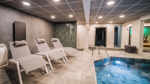 Ein moderner Poolbereich im Innenbereich mit Liegestühlen, einem Pool und einer gefliesten Decke.