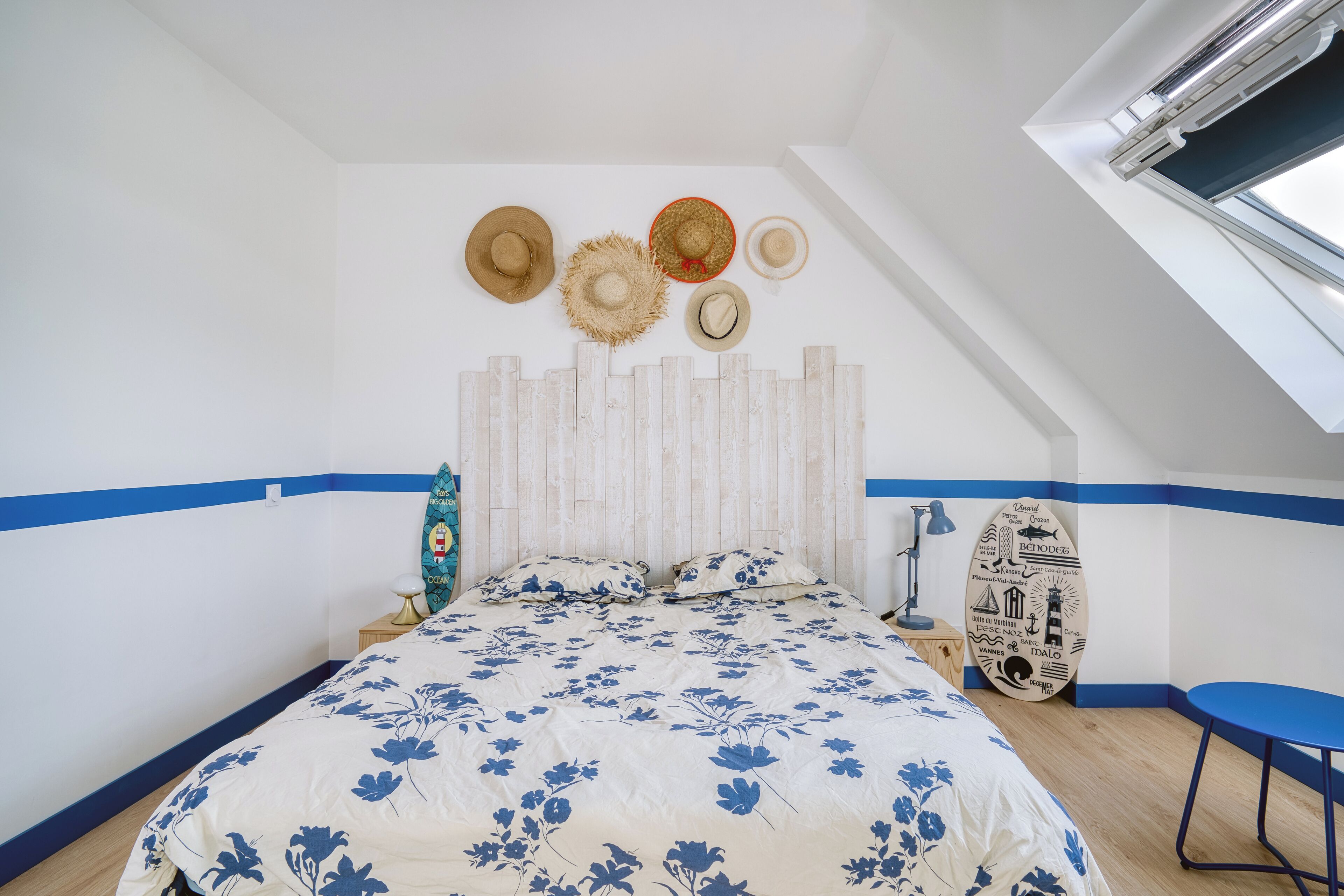 Una camera da letto con un letto, un comodino, una poltrona blu, una tavola da surf e una ventola a soffitto.