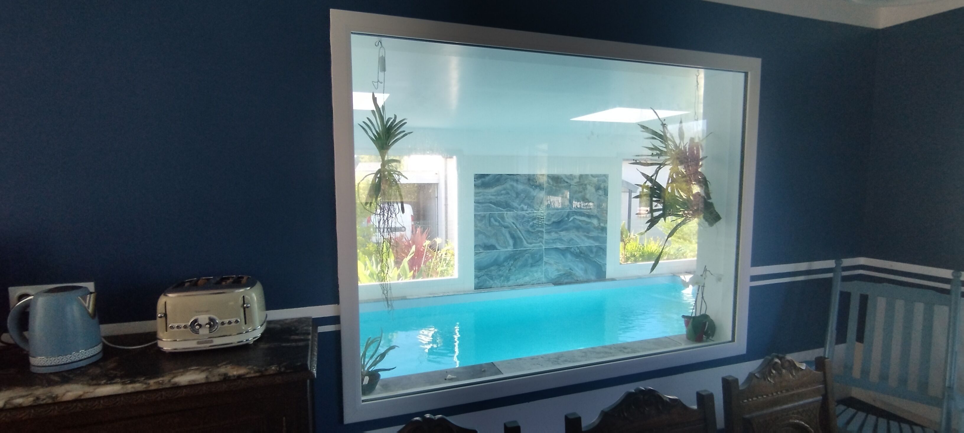 Ein Fenster mit Blick auf einen Swimmingpool, ein Toaster und ein Wasserkocher auf einer Arbeitsfläche.