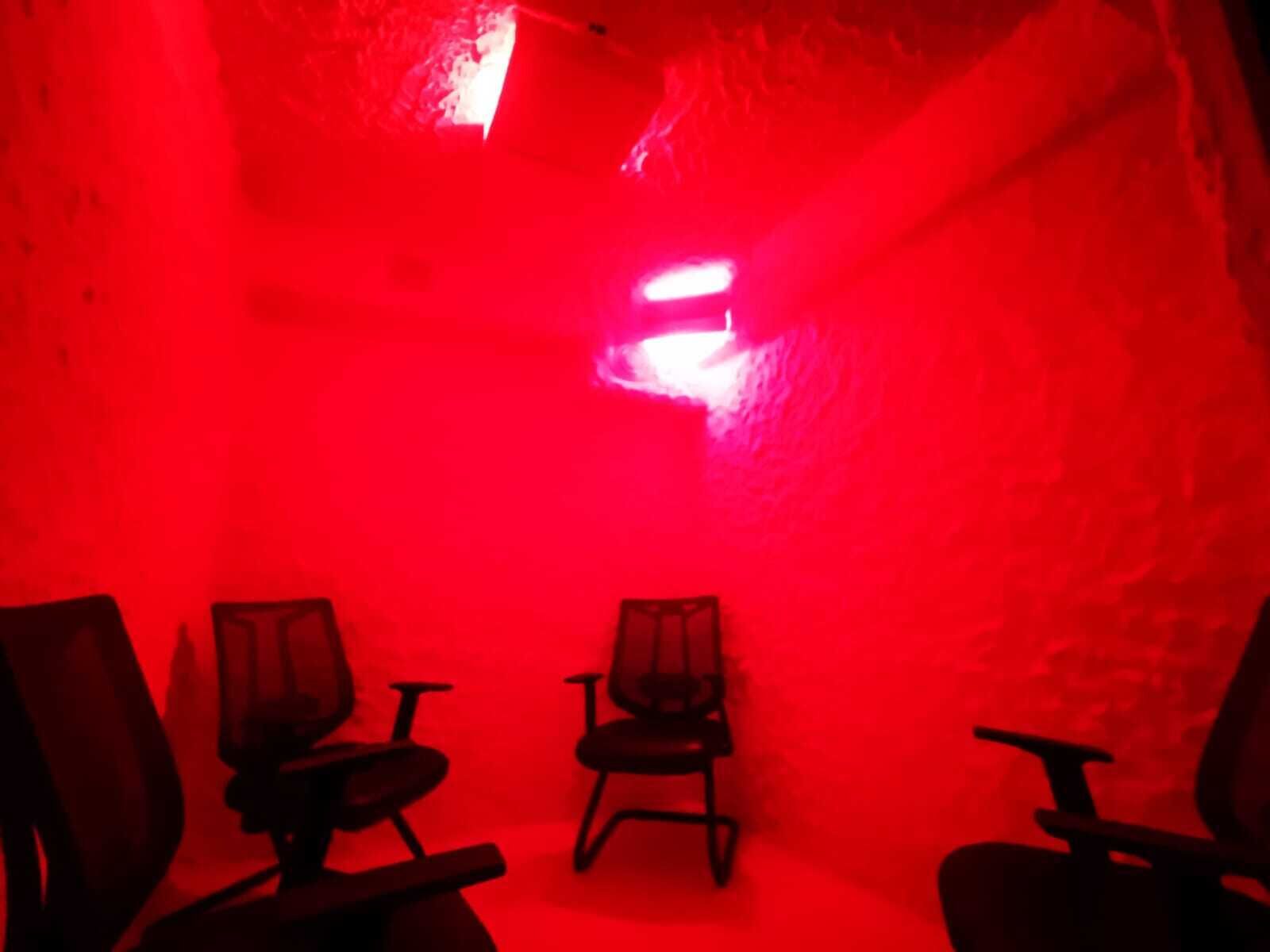 Une pièce dont l’intérieur est éclairé d’une lumière rouge, et qui contient trois chaises disposées en rangée.