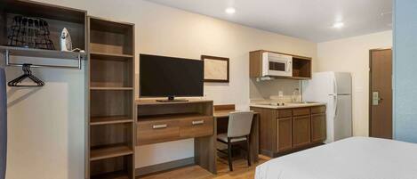 A compact hotel room with a bed, a desk with a chair, a TV, a microwave, and a refrigerator.