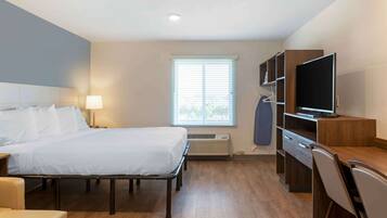 A hotel room with a bed, bedside table, lamp, TV, desk, chair, and a window with blinds.