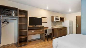 Ein kleines Hotelzimmer mit Bett, Schreibtisch mit Stuhl, Fernseher, Mikrowelle und Kühlschrank.