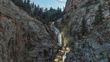 A natural rock formation with a waterfall cascading down a narrow gorge, surrounded by dense forest.