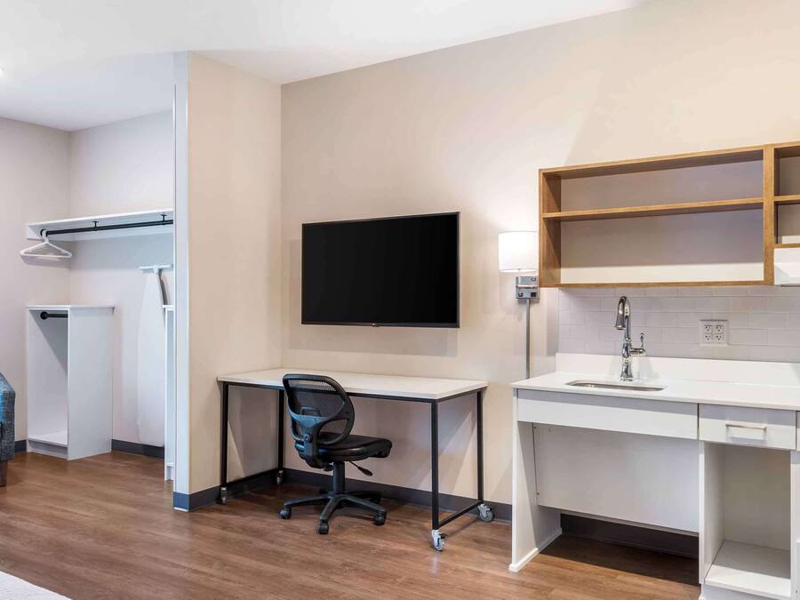 Une chambre d’hôtel moderne équipée d’un bureau, d’une chaise, d’une télévision et d’étagères intégrées.