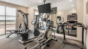 Une salle de sport équipée de divers appareils d’exercice, notamment des tapis de course, un appareil elliptique et une machine de musculation.