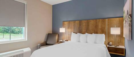 A hotel room with a large bed, two bedside lamps, a chair, and a window with a view of greenery.