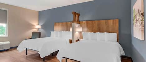 A hotel room with two beds, a wooden headboard, a desk, a chair, and a window.