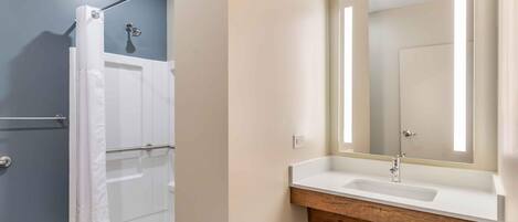 A modern bathroom with a shower, a sink with a wooden vanity, and a large mirror with a lighted frame.