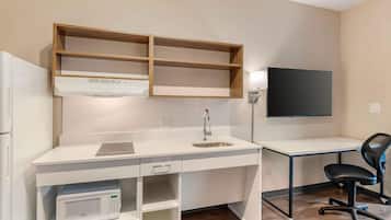 A compact kitchen with a microwave, a sink, and a wooden shelf above the countertop.