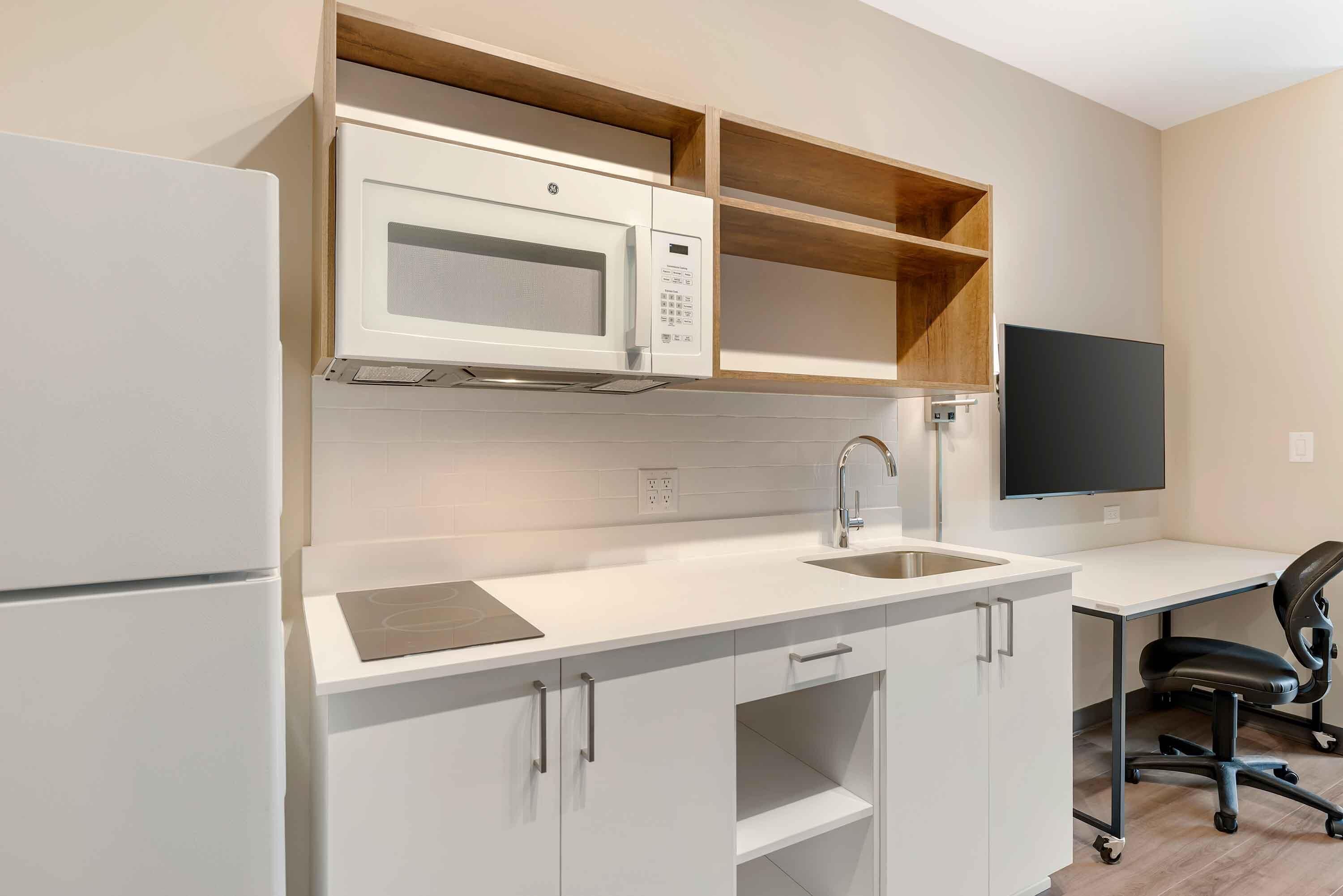 Une cuisine moderne avec des meubles blancs, un four à micro-ondes, un évier et un téléviseur à écran plat.