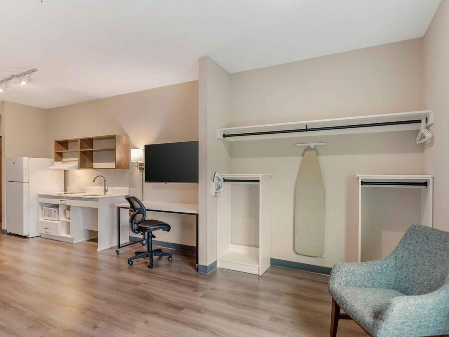 A modern apartment with a kitchenette, a desk, a chair, and a large mirror.