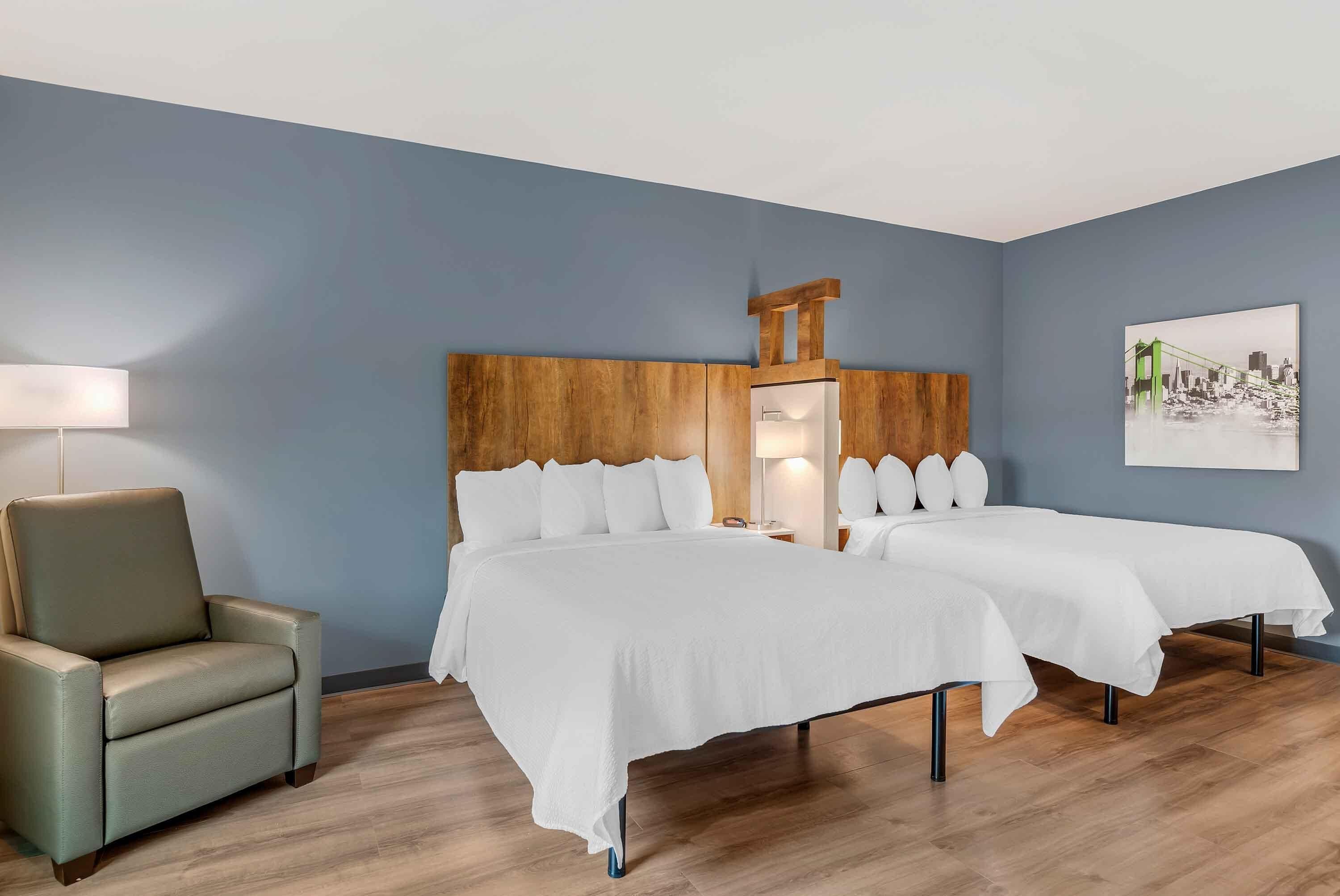 Una habitación de hotel con cabecera de madera, dos camas, una silla y una lámpara.