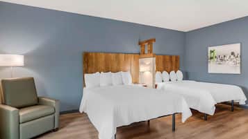 Una habitación de hotel con cabecera de madera, dos camas, una silla y una lámpara.