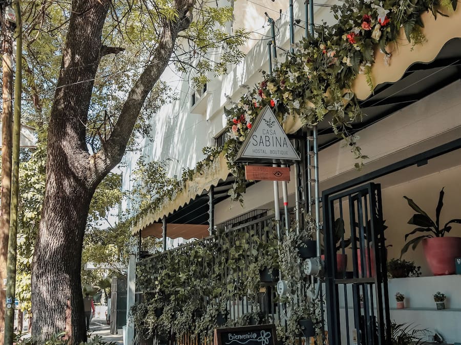 Vista de calle con un edificio identificado como 'Casa Sabina Hostel Boutique' y un cartel anunciando un restaurante de temática vintage.