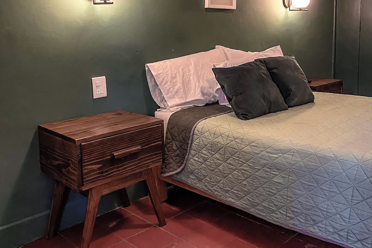 A bedroom with a bed, bedside tables, and wall-mounted lights.