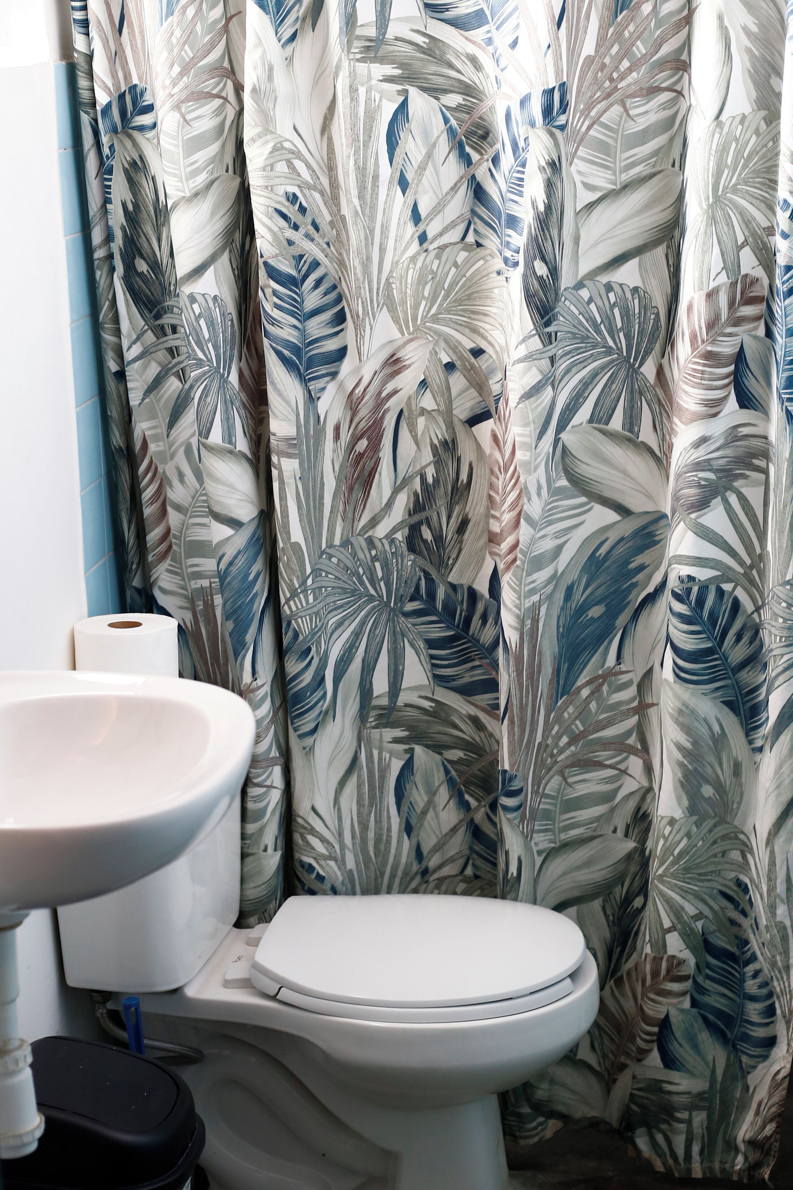 A bathroom with a toilet, sink, and a shower curtain with a leaf pattern.