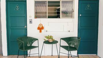 Two green doors with 'LAVANGERA' and 'BOSS' signs, a window, and two wicker chairs with a small table and a potted plant.